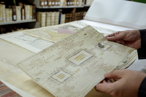 Zwei Hände halten eine Karte aus den historischen Beständen. Im Hintergrund sind weitere Karten erkennbar.