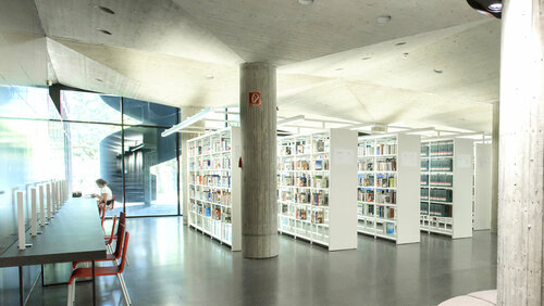 Ansicht im Erdgeschoss der GWLB. Regale im Hintergrund und Arbeitsplätze im Vordergrund.