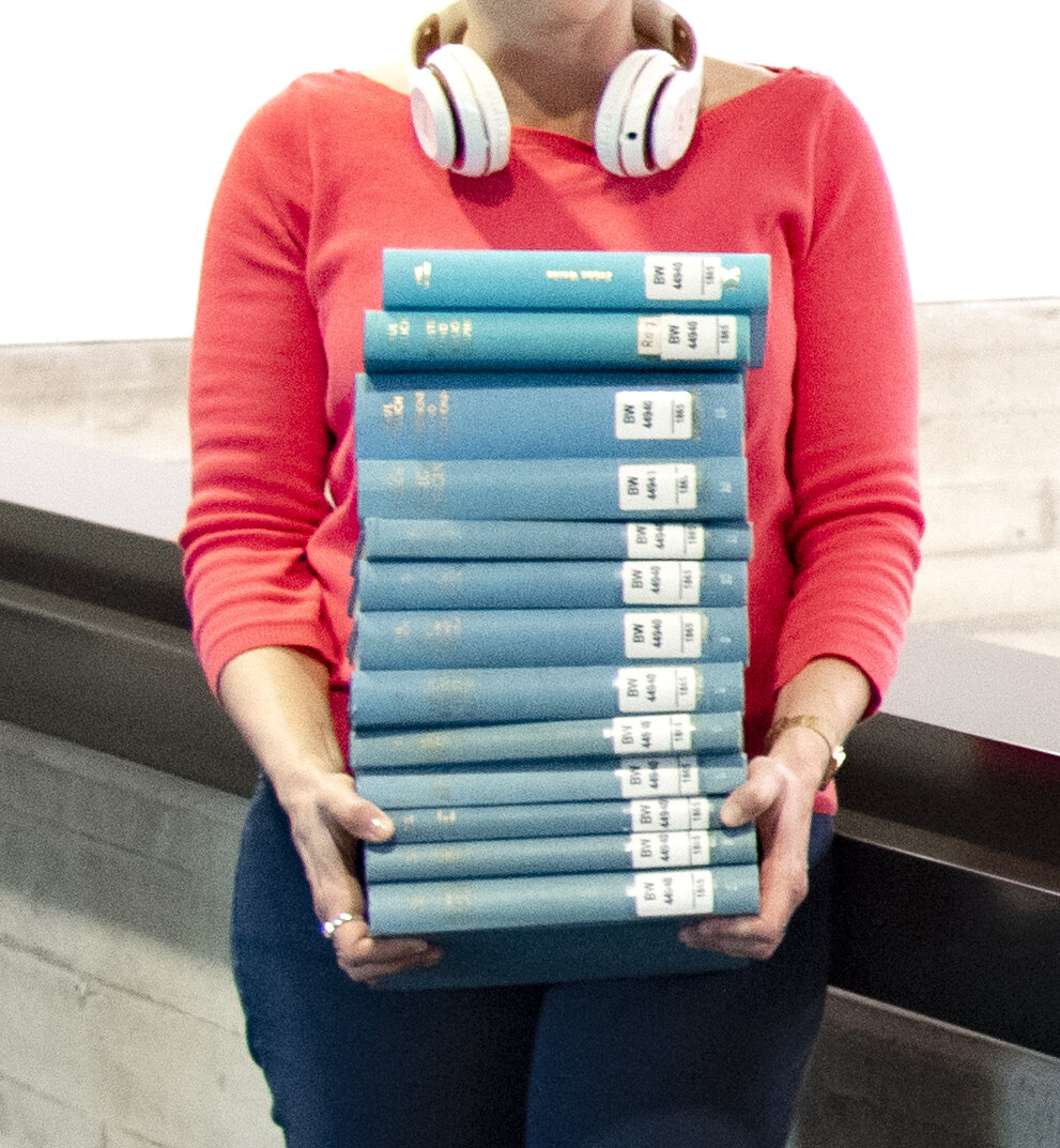 Eine Frau trägt einen großen Stapel Bücher.