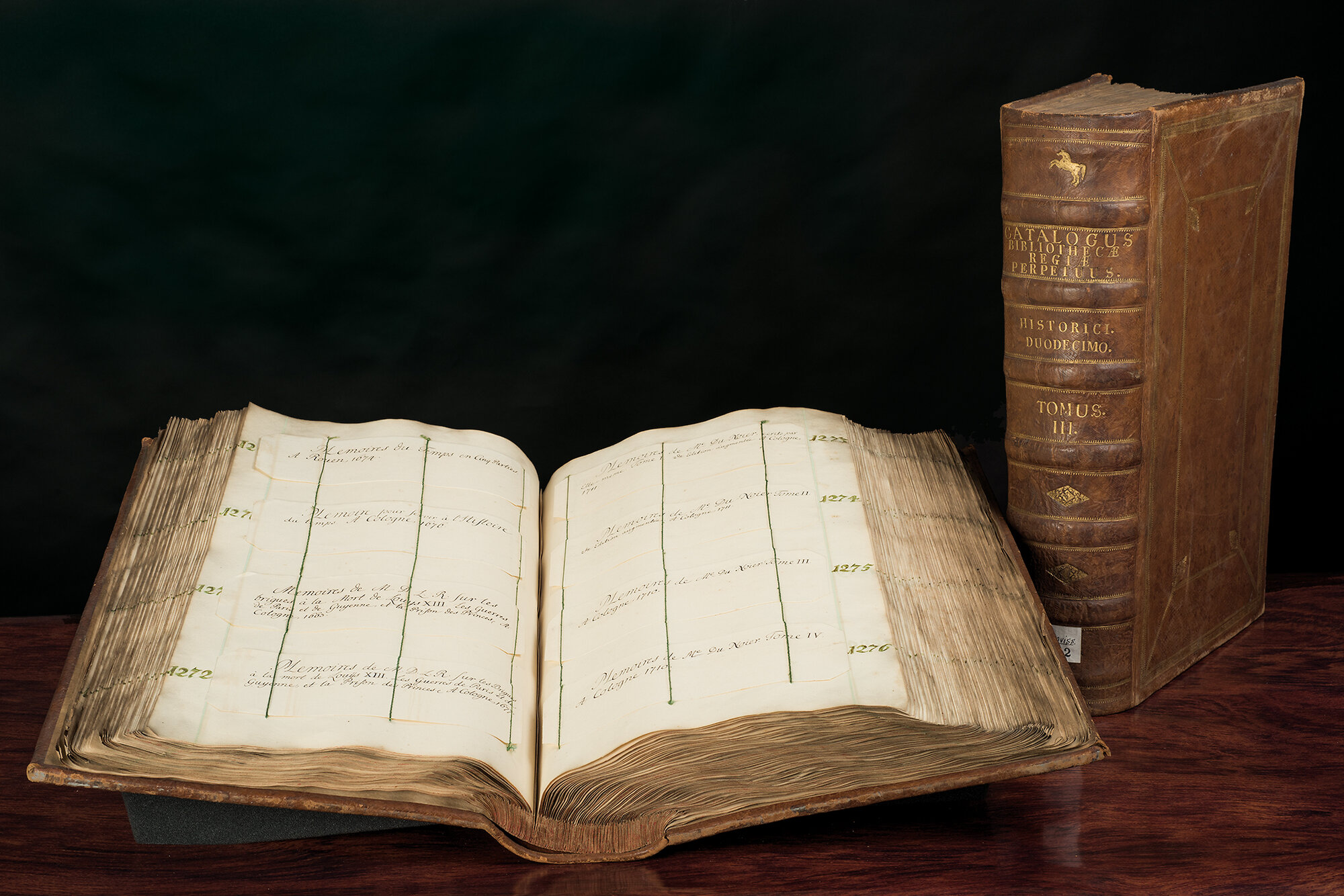 Aufgeschlagener Catalogus perpetuum bibliotheca regiae mit Buch im Hintergrund