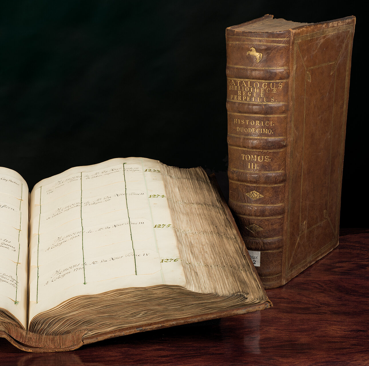 Aufgeschlagener Catalogus perpetuum bibliotheca regiae mit Buch im Hintergrund