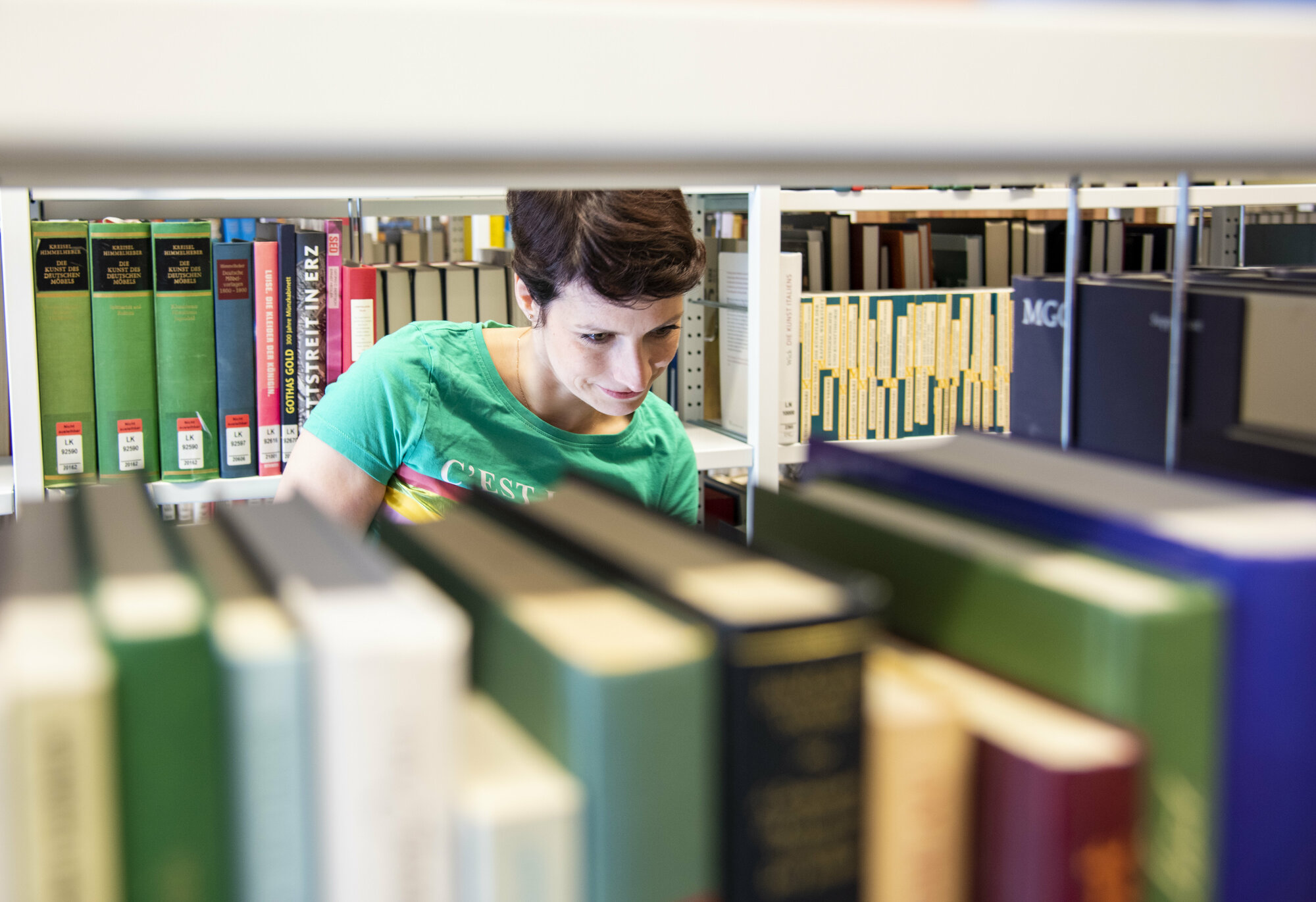 Eine junge Frau steht hinter Bücherregalen.