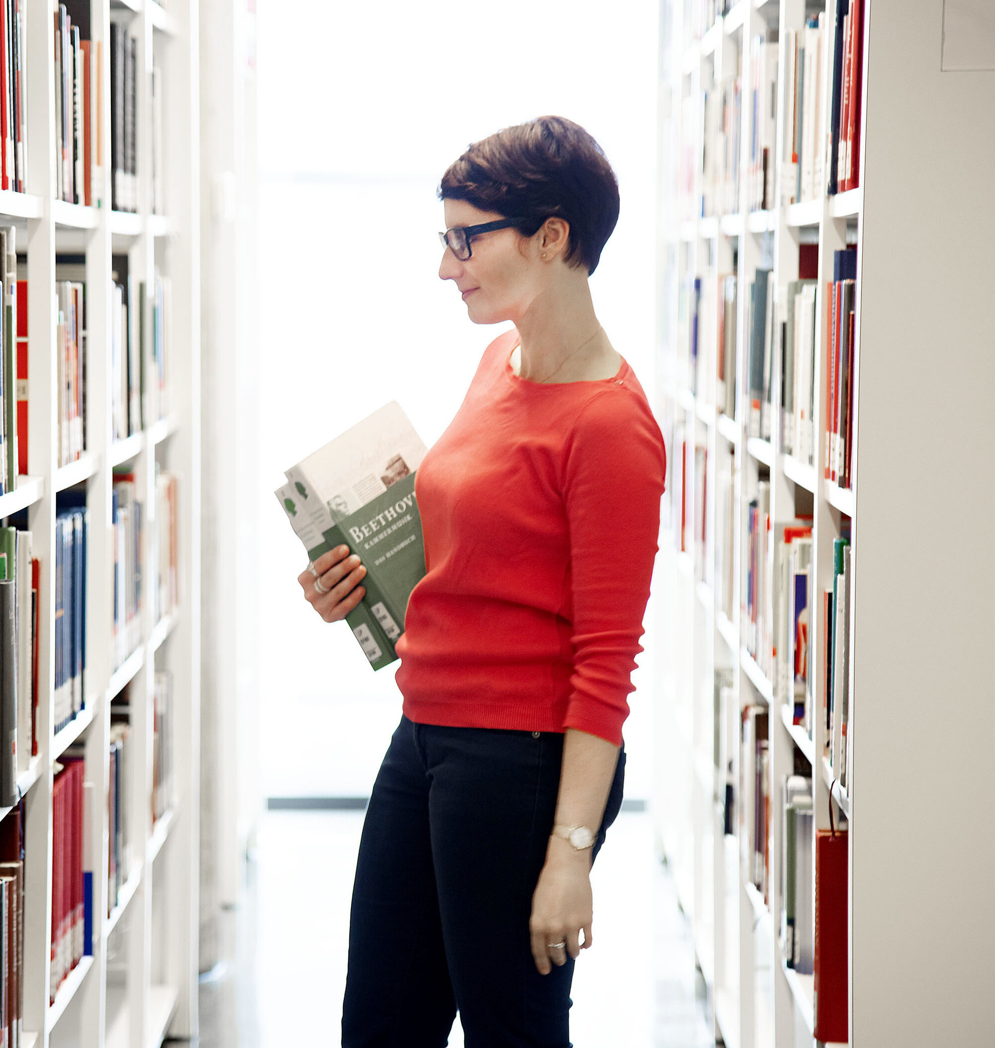 Ein Frau steht suchend zwischen zwei Bücherregalen.