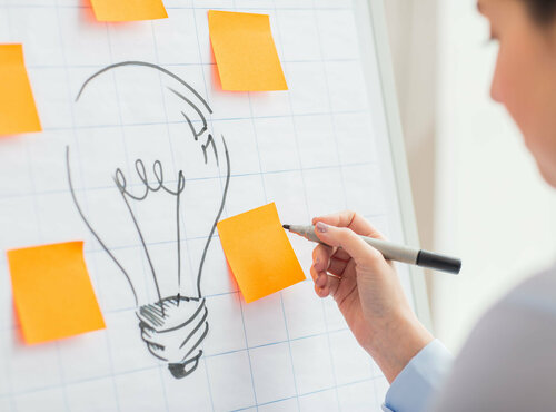 Person steht vor einer Flipchart. Darauf abgebildet ist eine Glühbirne.