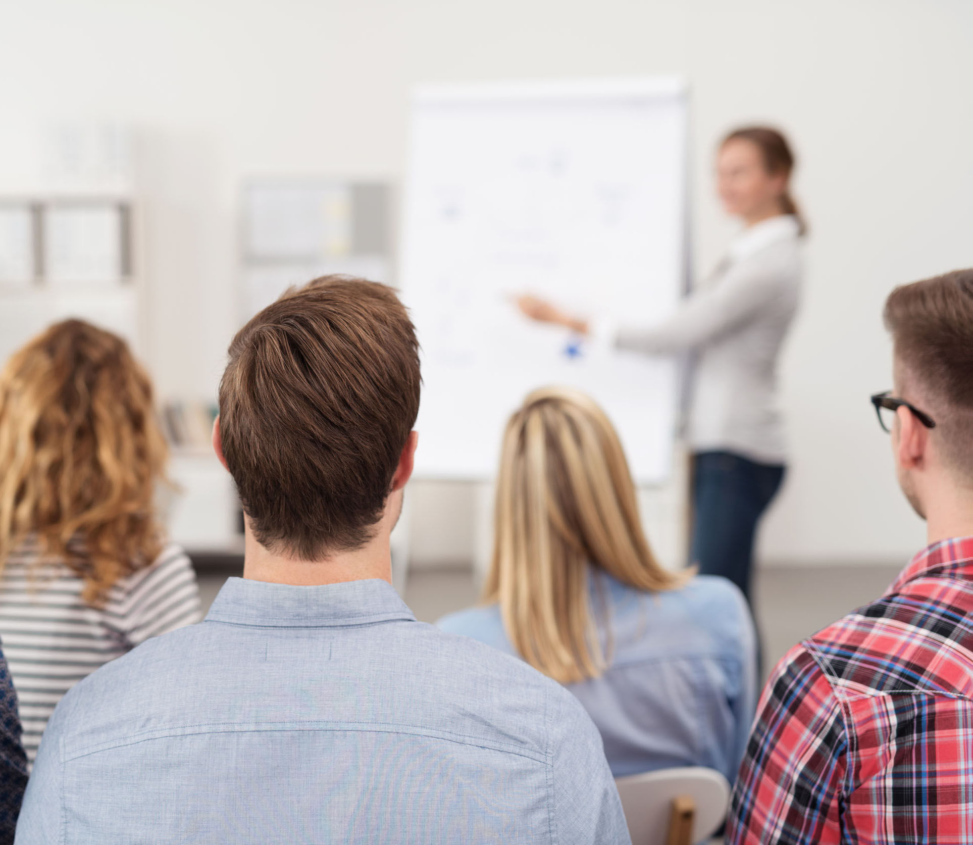 Eine Referentin, die an einer Flipchart steht, spricht vor einer Gruppe junger Menschen.